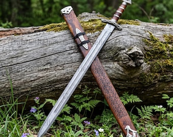 May include: A double-edged steel sword with a patterned blade and a brown leather-wrapped handle featuring silver-toned metal accents. The sword is paired with a matching brown wooden scabbard decorated with intricate carved knotwork patterns.