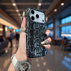 May include: A smartphone case featuring a textured, dark gray and black snakeskin pattern with a subtle glitter finish. The case has a rectangular cutout for a triple-lens camera system and is designed to fit a modern mobile device securely.