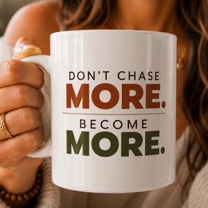 May include: A white ceramic mug featuring the text DON'T CHASE MORE. in brown and BECOME MORE. in dark green. The mug has a standard handle and a smooth, cylindrical body, displaying a motivational message printed in a clean, sans-serif font.