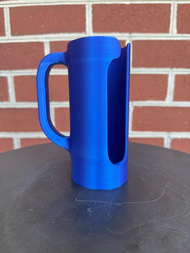 May include: A bright blue cylindrical object with a vertical cutout along one side and a curved handle attached to the exterior. The item features a smooth, solid-colored finish and a hollow interior, with a flat base and a rounded top edge.