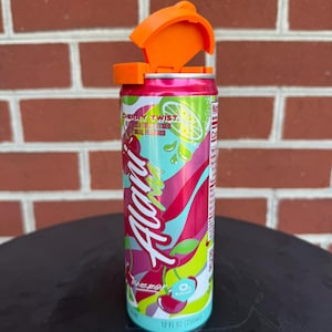 May include: A 12 fl oz aluminum energy drink can labeled Alani Nu Cherry Twist with a bright orange plastic flip-top lid attached to the top. The can features a colorful graphic design with red cherries, lime slices, and green accents on a pink background.