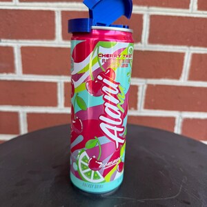 May include: A cylindrical Alani Nu energy drink can in Cherry Twist flavor with a bright pink, red, and light blue graphic design featuring cherries and lime slices. The can has a blue plastic flip-top lid attached to the top rim of the aluminum container.
