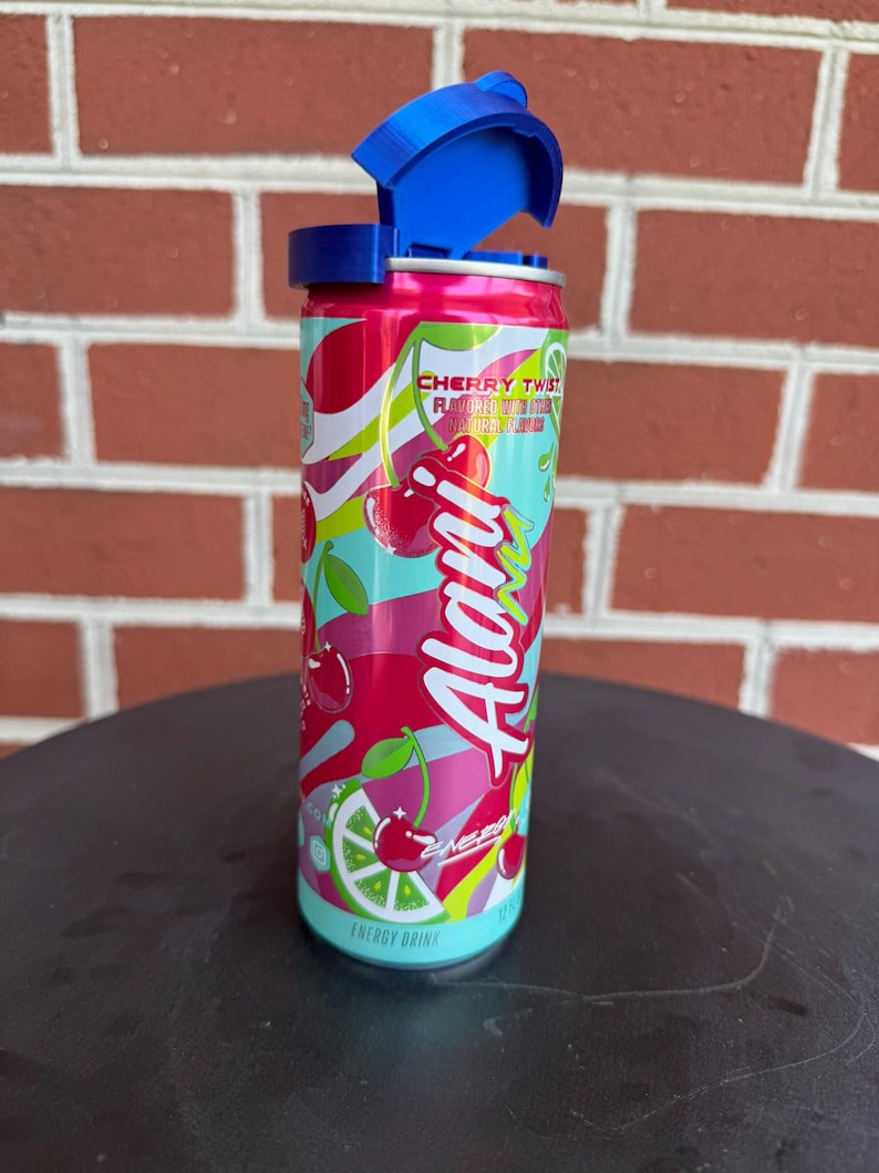 May include: A cylindrical Alani Nu energy drink can in Cherry Twist flavor with a bright pink, red, and light blue graphic design featuring cherries and lime slices. The can has a blue plastic flip-top lid attached to the top rim of the aluminum container.