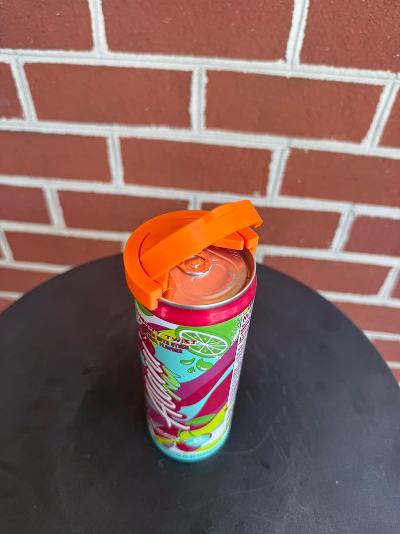 May include: A bright orange plastic beverage can handle attached to the top of a slim aluminum soda can. The can features a colorful label with green lime graphics, red and pink abstract shapes, and the visible text "Twist" in white lettering.