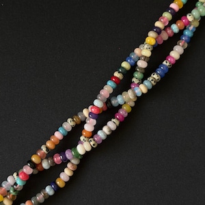 May include: A strand of small, round, multi-colored beads arranged in a random pattern. The beads feature a variety of translucent, opaque, and speckled finishes in shades of pink, blue, yellow, green, orange, purple, and black and white.