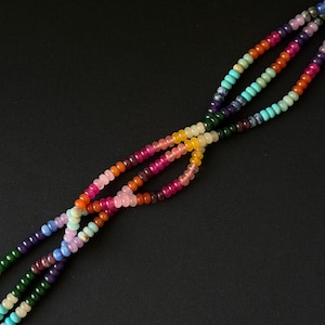 May include: A multi-strand necklace featuring small, round, translucent beads in a vibrant spectrum of colors including red, orange, yellow, green, blue, purple, and pink. The strands are twisted together to create a complex, interwoven pattern.