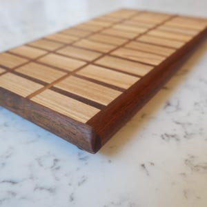 May include: A rectangular wooden serving board featuring a grid pattern of light tan wood segments separated by thin dark brown wood strips, framed by a solid dark brown wood border with rounded edges and a smooth, polished finish.