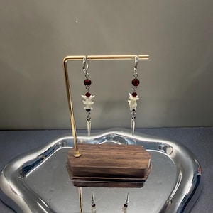 Può includere: Un paio di orecchini pendenti con ganci argentati, perline sfaccettate rosso scuro, piccoli segmenti bianchi simili a vertebre e punte metalliche argentate che pendono dalla parte inferiore di ciascun orecchino.