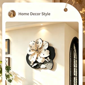 Puede incluir: Un reloj de pared con forma de flor blanca grande con manecillas y números negros. La flor está montada sobre un fondo negro texturizado con dos pequeños detalles de mariposas blancas. Aparece el texto Gentle Wind y Home Decor Style.