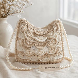 May include: A beige and cream crochet handbag featuring layered scalloped patterns and a pearl bead strap. The bag is adorned with small white pearls along the edges of the crochet layers and includes a rectangular tag labeled SoftraCrochetStudio.