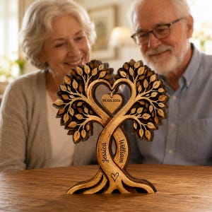 May include: A laser-cut wooden tree sculpture featuring two intertwined trunks engraved with the names Jessica and William, a small heart-shaped pendant hanging in the center with the date 06.06.2026, and a small heart icon engraved at the base.