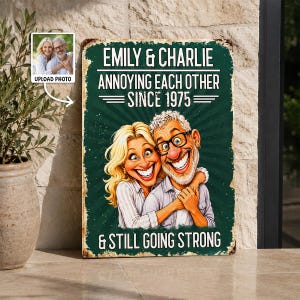 May include: A rectangular metal sign with a dark green background featuring a cartoon illustration of a couple. The text reads: EMILY & CHARLIE, ANNOYING EACH OTHER SINCE 1975, & STILL GOING STRONG. The sign has a distressed, weathered edge finish.