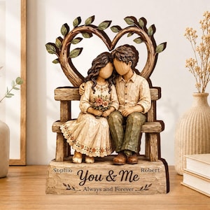 May include: A decorative figurine featuring a couple sitting on a wooden bench under a heart-shaped tree arch. The base is engraved with the names Sophia and Robert, the phrase You & Me, and the text Always and Forever in a carved wood style.