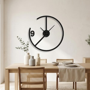May include: A black wall clock with a circular frame that is open at the top. The clock features a single large numeral nine on the left side, a central hub with three thin hands, and a straight vertical line extending from the centre to the top.