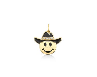 May include: A gold pendant shaped like a smiley face wearing a black cowboy hat. The hat features a band of small, clear, sparkling stones. The pendant has a small gold loop at the top for attachment to a chain or necklace.