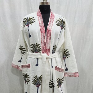 May include: A white waffle-textured robe featuring a repeating pattern of green palm trees with dark trunks. The garment includes a red and white chevron-patterned trim along the front opening, sleeve cuffs, and two front patch pockets, with a tie belt.