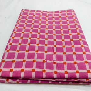 May include: A folded piece of fabric featuring a repeating grid pattern. The design consists of bright pink squares separated by thin white lines, with small, vibrant orange dots positioned at each intersection of the white grid lines.