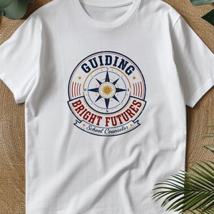 May include: A white short-sleeve t-shirt featuring a circular graphic on the chest. The design includes a compass rose in the center with the text "GUIDING BRIGHT FUTURES" and "School Counselor" printed in blue and red with a distressed finish.