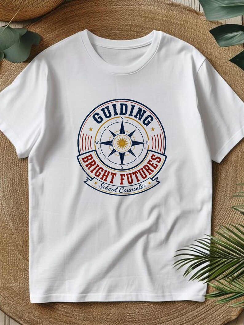 May include: A white short-sleeve t-shirt featuring a circular graphic on the chest. The design includes a compass rose in the center with the text "GUIDING BRIGHT FUTURES" and "School Counselor" printed in blue and red with a distressed finish.