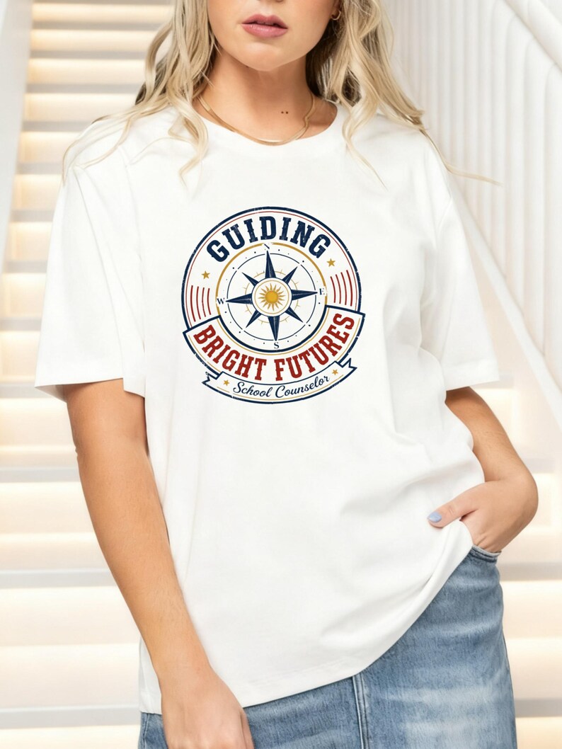 May include: A white short-sleeved t-shirt featuring a circular graphic with a compass rose in the center. The text reads "GUIDING BRIGHT FUTURES" in blue and red, with "School Counselor" in a banner below the compass design.