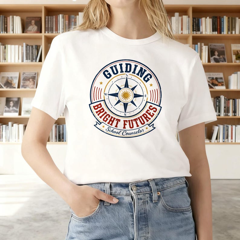 May include: A white short-sleeve t-shirt featuring a circular graphic with a compass rose in the center. The text reads "GUIDING BRIGHT FUTURES" in blue and red, with "School Counselor" written in blue script at the bottom of the design.