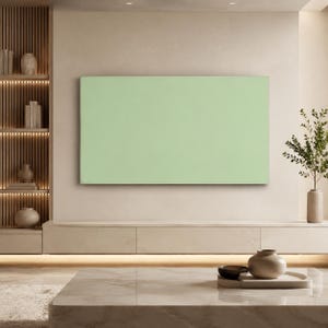Op de afbeelding: Een groot, rechthoekig, effen lichtgroen canvas kunstwerk dat centraal aan een muur is bevestigd. Het kunstwerk heeft een vlakke, uniforme pastelgroene kleur over het gehele oppervlak, wat zorgt voor een strak en eenvoudig visueel element.