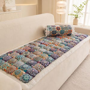 May include: A long, rectangular sofa cushion pad featuring a grid of square sections with a colorful, intricate mandala-style pattern in shades of blue, orange, and purple. A matching cylindrical bolster pillow rests on top of the seat cushion.