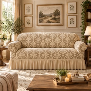 May include: A three-seat sofa featuring a beige and cream damask pattern fabric cover. The sofa has rounded arms, a tight back, and a solid cream-colored pleated skirt along the bottom edge. The upholstery covers the entire frame of the furniture.