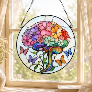 Op de afbeelding: Een ronde glas-in-lood zanger in de vorm van een menselijk brein, samengesteld uit kleurrijke bloemen in roze, paarse, oranje en groene tinten. Een regenboogkleurige steel strekt zich naar beneden uit, omringd door kleine vlinders in roze, blauw en oranje.