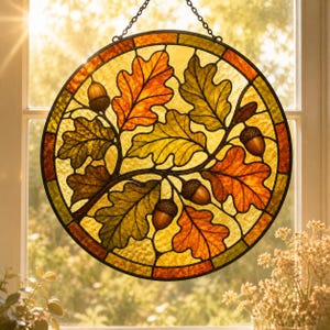 May include: A circular stained glass suncatcher featuring a detailed pattern of oak leaves and acorns in shades of amber, orange, yellow, and green. The design is enclosed within a dark metal frame and suspended by a metal chain for hanging.