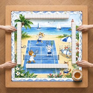 Pode incluir: Uma mesa de mahjong quadrada com moldura de madeira apresentando um tapete estampado de gatos jogando tênis em uma praia. O tapete exibe uma quadra de tênis azul, palmeiras, um farol, veleiros e uma mesa com bebidas. Peças brancas estão dispostas.