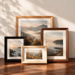 May include: Four framed landscape prints featuring nature scenes. One large print shows misty mountains, a medium print shows a lake with a wooden pier, a small vertical print shows a rocky coastline, and a small horizontal print shows an autumn forest.