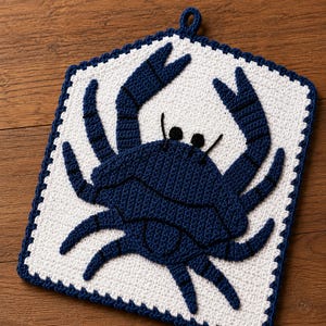 May include: A square crochet potholder featuring a dark blue crab motif centered on a white background. The potholder has a dark blue border and a small loop at the top for hanging. The crab design is detailed with dark blue yarn and black accents.