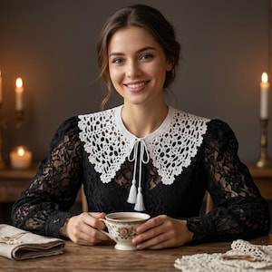 May include: A black long-sleeved lace top featuring a detachable white crocheted collar with a tie closure and tassel ends. The collar has an intricate openwork pattern, and the garment is worn with a floral patterned ceramic teacup.