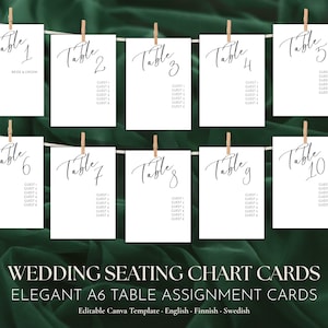 May include: Ten white rectangular table assignment cards hanging from a string with wooden clips. Each card features black cursive text reading Table 1 through Table 10, with printed guest list placeholders below the table numbers in a simple sans-serif font.