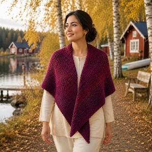May include: A deep burgundy, chunky knit triangular shawl with a textured garter stitch pattern. The shawl is draped over a light beige long-sleeved top and matching trousers, creating a layered look with a soft, thick yarn construction.