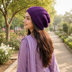 May include: A deep purple knit beanie featuring a ribbed texture and a slouchy fit. The hat is constructed with a wide, folded brim and vertical knit lines that extend from the base to the crown, creating a consistent pattern throughout the fabric.