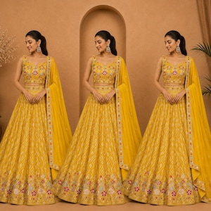 May include: A vibrant yellow lehenga set featuring a sleeveless blouse and a floor-length skirt, both adorned with intricate multi-colored floral embroidery and mirror work. A matching sheer yellow dupatta with a decorative border completes the set.