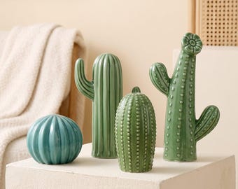 May include: A set of four green ceramic cactus figurines in various shapes and sizes. One is a round teal sphere, one is a tall ribbed column, one is a textured oval with small dots, and one is a tall cactus with a flower on top.