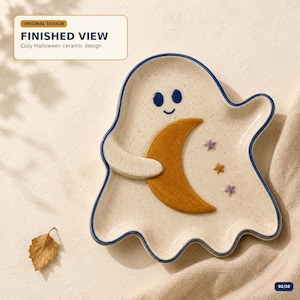 Puede incluir: Un plato de cerámica con forma de fantasma, acabado en color crema moteado y borde azul oscuro. El fantasma tiene una cara sonriente, sostiene una gran luna creciente naranja entre sus brazos y presenta tres pequeñas estrellas moradas y amarillas.