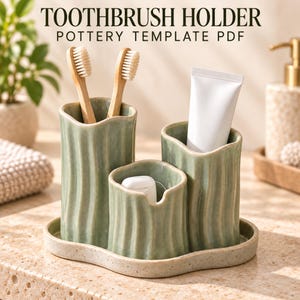 May include: A sage green ceramic toothbrush holder set with three vertical compartments of varying heights on a matching oval tray. The text TOOTHBRUSH HOLDER POTTERY TEMPLATE PDF is visible at the top. Two bamboo toothbrushes, a white tube, and dental floss are inside.