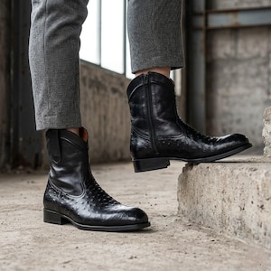 May include: A pair of black leather ankle boots featuring a textured ostrich-skin pattern on the lower portion, a smooth leather upper shaft, a side zip closure, a rounded toe, and a low stacked heel, worn with grey textured trousers.
