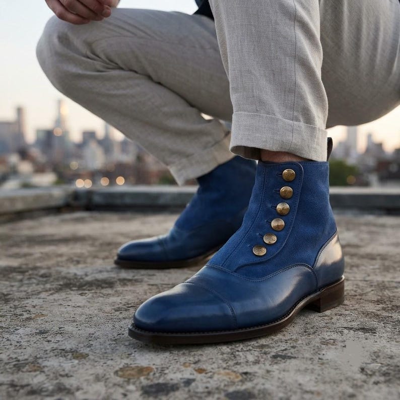 Men's blue leather cap-toe button boots worn with grey wool trousers on a rooftop.