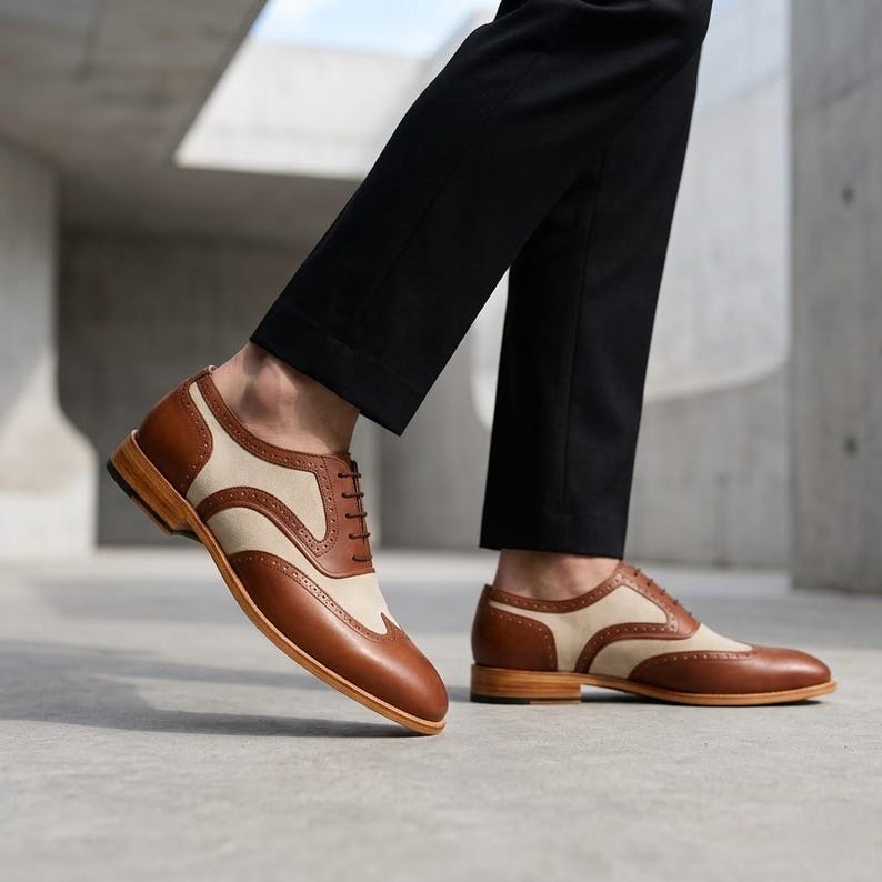 Side view of men's two-tone spectator shoes in brown leather and beige canvas on a concrete background.