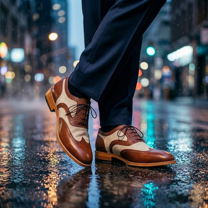 Men's spectator shoes reflected in a rain-slicked city street with colorful bokeh lights.