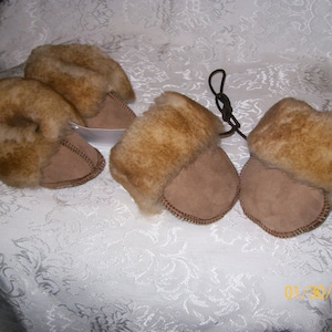 May include: Four pairs of brown suede baby booties with fur trim. The booties are tied together with a brown cord.