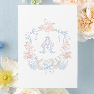 Puede incluir: Una tarjeta rectangular blanca con una ilustración central de corona floral en tonos pastel rosa y azul, rodeando un monograma decorativo con las letras AG. La tarjeta incluye el texto ENCRESTUDIO DESIGN&PRINT en la esquina superior izquierda.