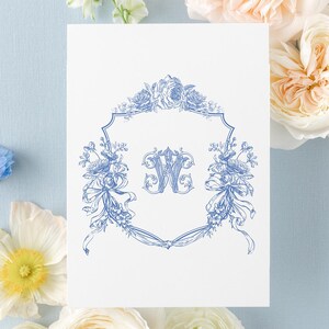 May include: A white rectangular card featuring a blue ink illustration of a decorative crest with a central letter W, surrounded by floral motifs and ribbons. The text ENCRESTUDIO DESIGN&PRINT is printed in the upper left corner of the card.