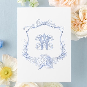 May include: A white rectangular card featuring a blue ink illustration of a decorative crest with a central letter W, surrounded by floral motifs and a ribbon bow at the top. The text ENCRESTUDIO DESIGN&PRINT is visible in the upper left corner.