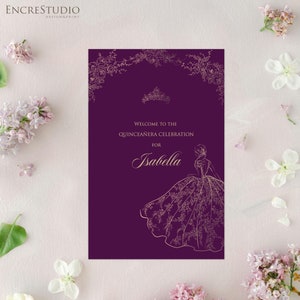 Puede incluir: Invitación morada con borde floral dorado y una silueta dorada de una mujer con un vestido de gala. El texto dice "Bienvenido a la celebración de Quinceañera para Isabella".